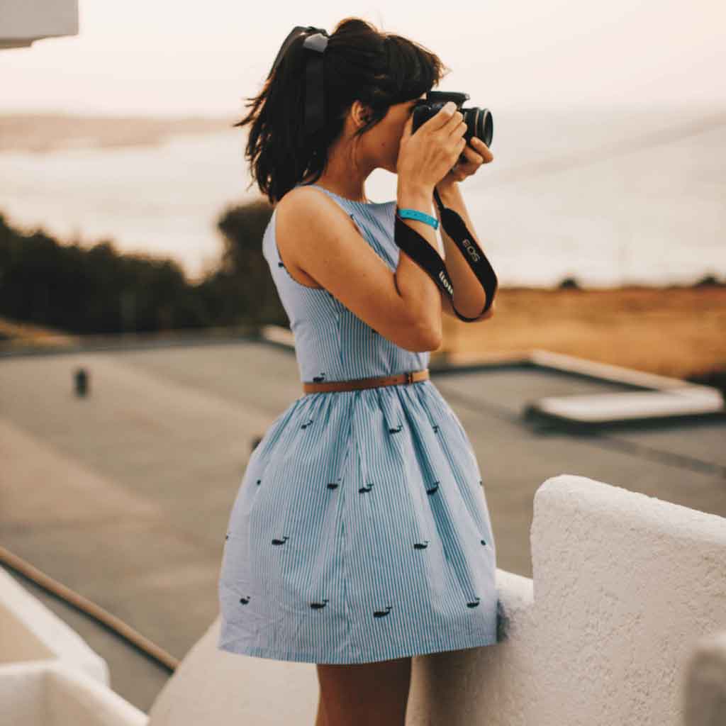 A stylish woman in a blue summer dress photographing a serene coastal view